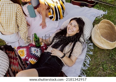 A young girl of Asian beauty lies on a blanket with a beer in her hand.