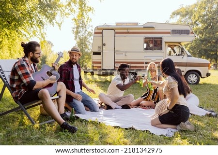 Group of young friends spending time on the camper side on drinking beer