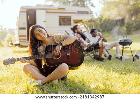 A young girl of Asian beauty plays the guitar. Friends spend time together in nature traveling in an RV