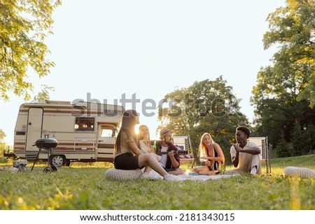 A group of college friends spend time together traveling in a camper van. A bearded middle-aged boy plays guitar.