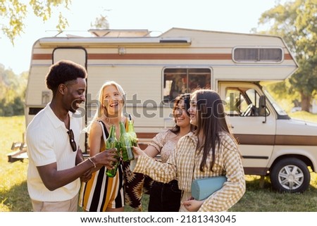Group of young friends spending time on the camper side on drinking beer