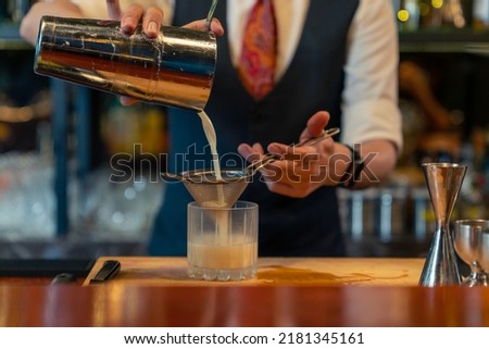 Male bartender preparing and pouring mixed beverage cocktail drink from shaker into cocktail glass on bar counter at pub. Professional barman making alcoholic drink serving to customer at nightclub Royalty-Free Stock Photo #2181345161