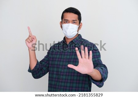 Adult Asian man wearing medical mask pointing finger up Royalty-Free Stock Photo #2181355829