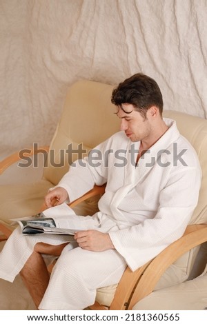 Young man in a white bathrobe relaxing in a salt room and reading