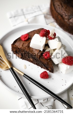 piece of chocolate round brownie on plate with ice cream and raspberries, appetizing dessert or sweets, white background, close up