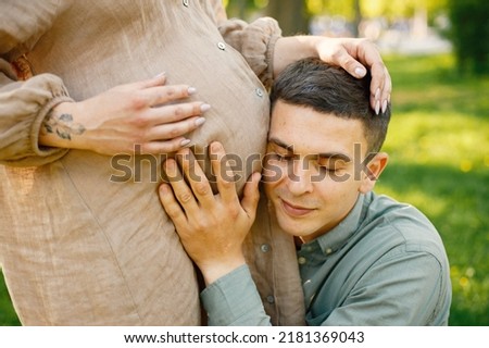 Cropped photo of a man hugging pregnant belly of wife in park