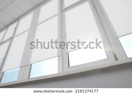Large window with white roller blinds indoors, low angle view Royalty-Free Stock Photo #2181374177