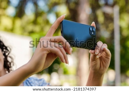 Young beautiful woman wearing summer dress on city park, outdoors taking horizontal photo with her smart phone.