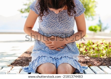 Young beautiful woman wearing summer dress on city park, outdoors with hand on stomach because indigestion, painful illness feeling unwell. Ache or pregnancy concept. Royalty-Free Stock Photo #2181374483