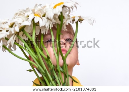 A cute boy with a beautiful bouquet of large daisies. Portrait of a child, funny and cute facial expression. Selective focus. A postcard for the celebration of the day of family, love and fidelity.