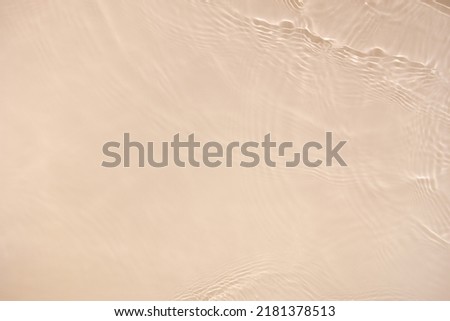 Transparent beige clear water surface texture with ripples, splashes. Abstract nature background Water waves in sunlight with copy space, top view. Cosmetic moisturizer micellar toner emulsion Royalty-Free Stock Photo #2181378513