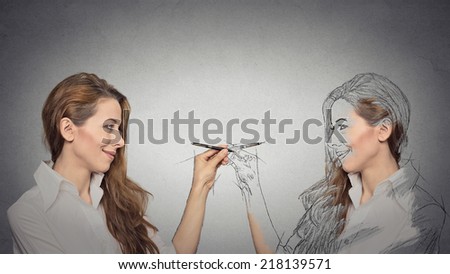 Create yourself, your future destiny, image, career concept. Attractive young woman drawing a picture, sketch of herself on grey wall background. Human face expressions, determination, creativity