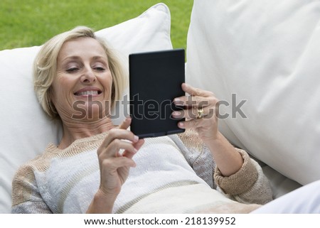 Senior woman laying on outdoor sofa and using digital tablet