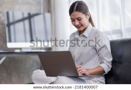 Happy Asian teen girl using laptop computer on the sofa, Smiling young woman using apps, shopping online, reading news, browsing the internet.