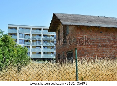 Fenced single-family house made of brick, not covered with plaster and in the background a new apartment building