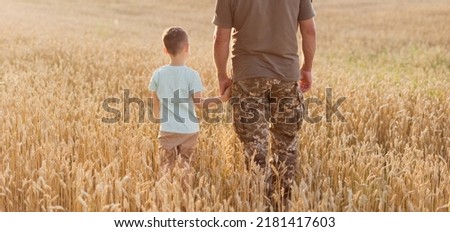 Military man and child holding hands in wheat field at sunset. Ukraine independence day concept. Stop war in Ukraine. Save Ukraine