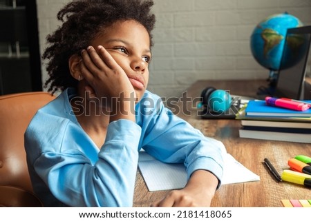 Sad bored African-American girl doing homework at home at her desk. Back to school concept. School distance education, home schooling, diverse people. 