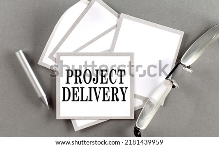 PROJECT DELIVERY text written on sticky with pencil and glasses
