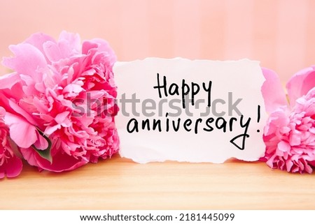 Happy anniversary - card with greeting lettering and bouquet of pink peony flowers on rosy background