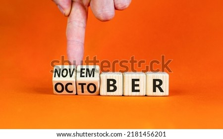 Symbol for the change from October to November. Businessman turns wooden cubes and changes the word 'October' to 'November'. Beautiful orange background, copy space. Happy November concept.