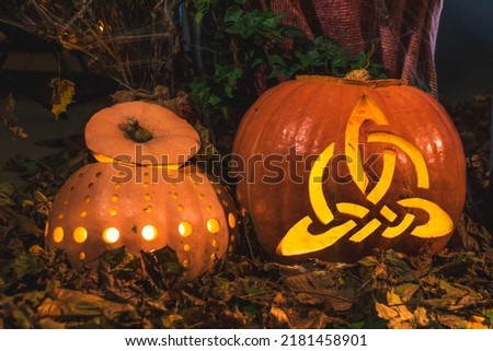 Halloween composition with carved triquetras on pumpkins. Halloween holiday in a misty forest with an arrangement of glowing pumpkins and dried leaves Royalty-Free Stock Photo #2181458901