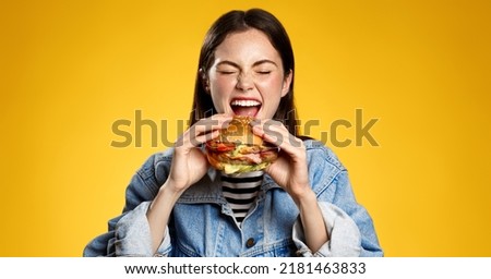 Girl bites cheeseburger with pleasure. Woman eating hambuger, order burger for takeaway food delivery at fastfood restaurant Royalty-Free Stock Photo #2181463833