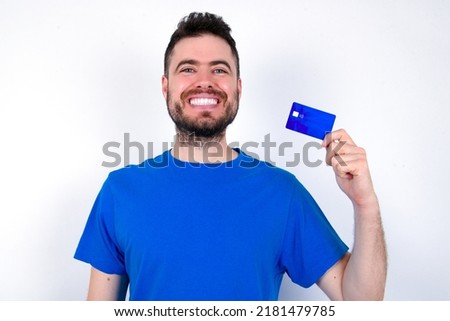 Photo of happy cheerful smiling positive Young caucasian man wearing blue T-shirt over white background recommend credit card