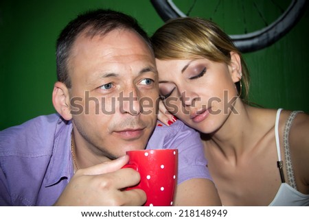 The photo shows a young man and a young woman. They sit at a table in his hands a cup.