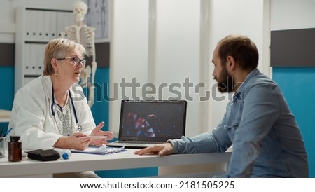 Female medic looking at coronavirus illustration on laptop with sick patient, talking about medication and prevention. Virus animation on display to cure disease in medical cabinet.