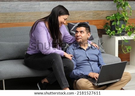 Latino adult man and woman couple use their laptop in the living room to shop online, make payments, plan trips, view photos and make video calls