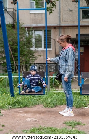 A mother rocks her baby on a swing in the yard