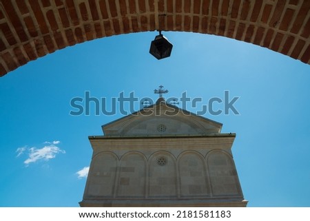The Top Part of a Church Pictured under a Brick Arch with an Ornament Hanging Below