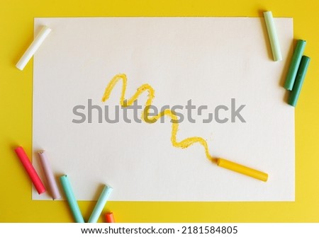 The curved line is drawn in yellow pastel chalk on a white sheet. Soft pastel and a sheet of paper on a yellow background. Top view Royalty-Free Stock Photo #2181584805