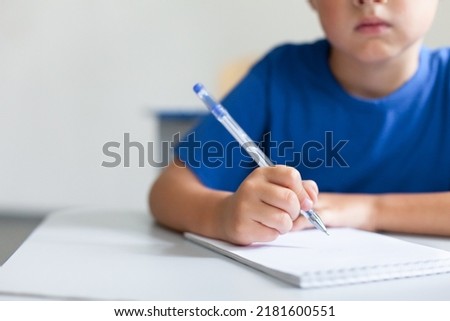 Writing hand of school child on lesson. Pupil sitting at desk in classroom. Kid studying in elementary college. Primary student back to school. Education for children. Close up of pen and copybook Royalty-Free Stock Photo #2181600551