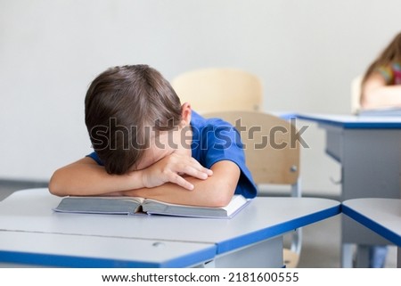 School child sleeping on boring lesson. Tired pupil learning to read book. Sleepy kid sitting at desk in classroom in elementary college. Primary student back to school in early morning Royalty-Free Stock Photo #2181600555