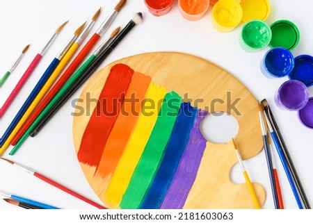 palette, paints, brushes on a white table. LGBT flag and colors