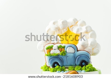 Birthday cake for a one year old kid. White cake decorated with green edible grass and gingerbread cookies in the shape of a truck and digit one. Fluffy cloud shaped meringue cookies on top of cake