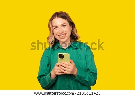 A photo of happy woman holding her phone and smiling at the camera