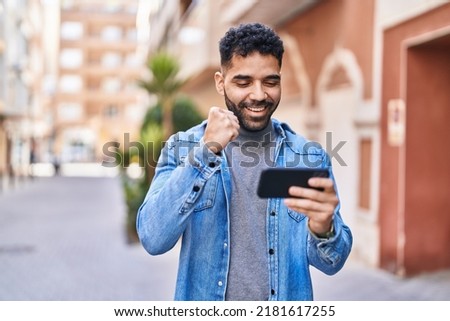 Young hispanic man smiling confident playing video game at street Royalty-Free Stock Photo #2181617255