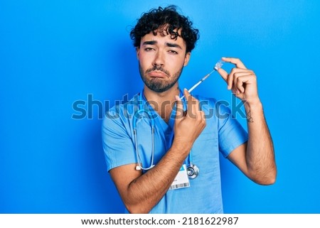 Young hispanic man wearing nurse uniform holding vaccine depressed and worry for distress, crying angry and afraid. sad expression. 