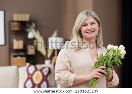 Happy elderly grandmother looks into the camera with a smile holding white roses flowers mature woman got a mother's day gift March 8, smiling mature female excited about the surprise.