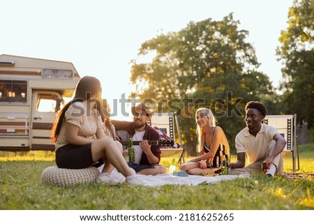 A group of college friends spend time together singing surrounded by nature. A bearded middle-aged boy plays the guitar. The good friends travel together in their beloved old camper van.
