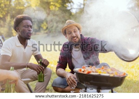 Two guys are preparing a barbecue for friends. Good friends have come to relax in nature