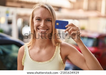 Young caucasian woman holding credit card looking positive and happy standing and smiling with a confident smile showing teeth 