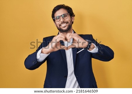 Handsome latin man standing over yellow background smiling in love doing heart symbol shape with hands. romantic concept. 