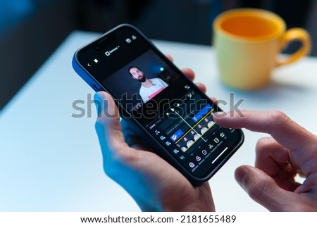 the video editor program on the phone. A young man is editing a video on his phone Royalty-Free Stock Photo #2181655489