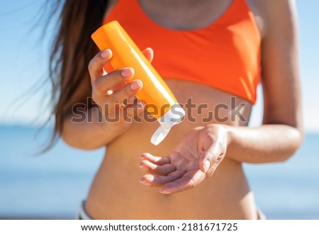a girl in a bathing suit on the beach smears her body with sunscreen protective from the sun