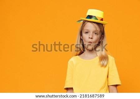 a cute, funny girl, of school age, stands on a yellow background in a yellow T-shirt in a straw hat. Horizontal studio photography with blank space for advertising mockup