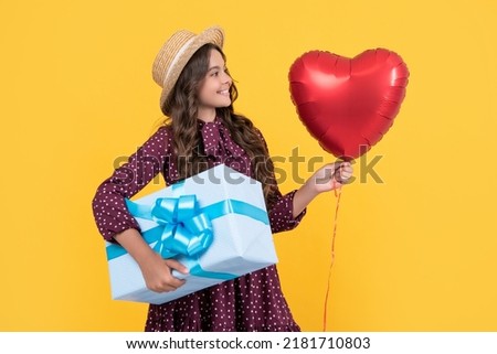 happy teen child with red heart balloon and present box on yellow background