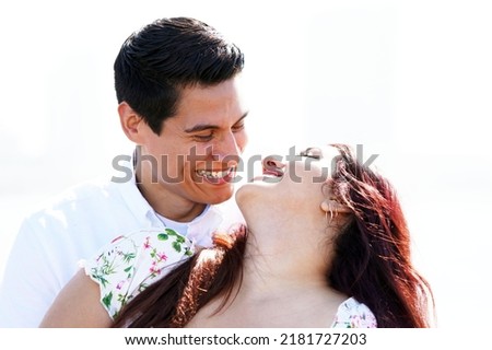 Attractive couple leans into one another to smile lovingly outside on a sunny morning                              